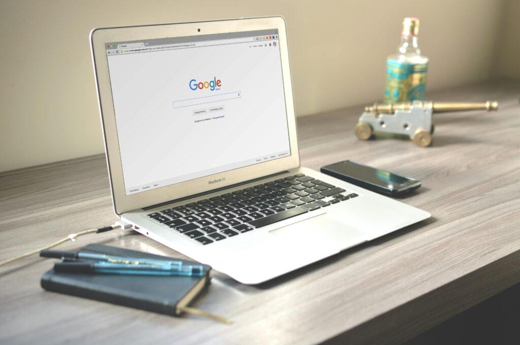 MacBook Air displaying Google homepage on desk with smartphone and notebook, illustrating modern digital marketing workspace